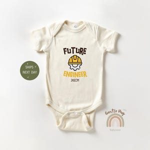 May include: A cream colored baby onesie with the text "FUTURE ENGINEER" in brown and yellow. A yellow hard hat icon is above the text. The name "JASON" is printed below the text.