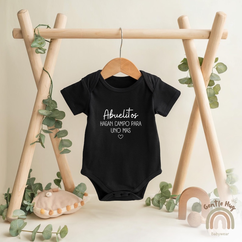 K&ouml;nnte beinhalten: Schwarzer Baby Strampler mit wei&szlig;em Text, der "Abuelitos hagan campo para uno mas" mit einem kleinen Herzsymbol lautet.