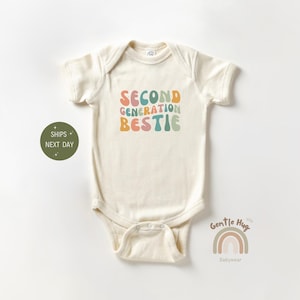 May include: A white baby onesie with the text "Second Generation  Bestie" in colorful, retro-style lettering.