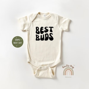May include: A white baby onesie with black text that reads "BEST BUDS" in a retro font.