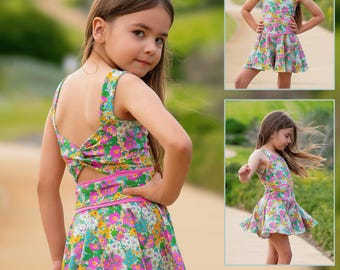 Puede incluir: Un vestido, falda pantalón o pelele con estampado floral, cuerpo sin mangas, detalle de espalda retorcida y cintura ancha. La tela muestra un patrón vibrante de flores rosas, amarillas y azules sobre fondo claro. El texto dice Ember.