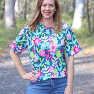 Pode incluir: Uma mulher vestindo uma camisa de manga curta com estampa floral azul e rosa com jeans azul.