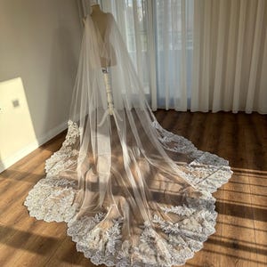 May include: A white tulle wedding veil with a delicate lace trim. The veil is draped over a dress form and has a long train.