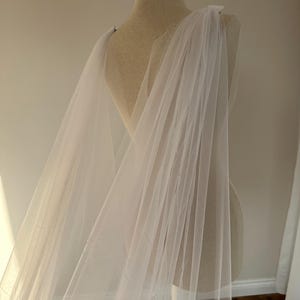 May include: A white tulle wedding veil draped over a dress form. The veil is sheer and delicate, with a soft, flowing texture.