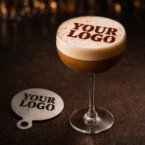 Puede incluir: Un cóctel en una copa con una capa espumosa, con el texto "YOUR LOGO" espolvoreado en la parte superior. Una plantilla a juego con el mismo texto se encuentra al lado del vaso. La bebida es marrón con una capa de espuma blanca.
