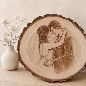 Peut inclure: Une tranche de bois circulaire présentant une illustration gravée au laser d'un couple s'enlaçant. L'image montre une personne en robe de mariée avec un voile et une personne en costume, en vue de profil avec une texture de grain de bois visible.