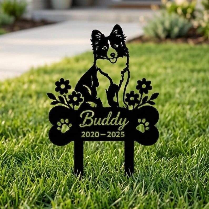 Op de afbeelding: Een zwarte metalen tuinpaal met het silhouet van een hond boven een botvormig plaatje. Het plaatje toont de naam Buddy en de jaren 2020-2025, geflankeerd door twee pootafdrukken en decoratieve bloemmotieven aan weerszijden.