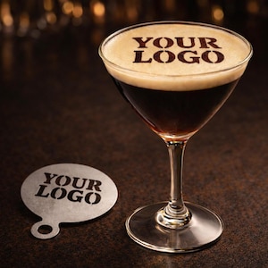 Può includere: Un bicchiere da martini riempito con una bevanda marrone scuro, sormontato da uno strato schiumoso. Il testo "YOUR LOGO" è stampato sulla schiuma. Un sottobicchiere abbinato con lo stesso testo è accanto al bicchiere. La bevanda è su una superficie marrone scuro.