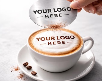 May include: A white ceramic coffee cup and saucer with a cappuccino. The cappuccino has a design on top with the text "YOUR LOGO - HERE". A silver disc with the same text is held above the cup. Coffee beans are scattered around the cup.