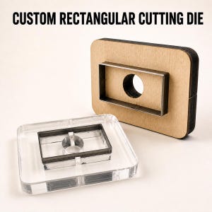 Pode incluir: Uma matriz de corte retangular personalizada com uma base de madeira, uma lâmina de metal e um recorte central circular, acompanhada por um bloco de acrílico transparente com uma lâmina de metal retangular correspondente e um inserto circular.