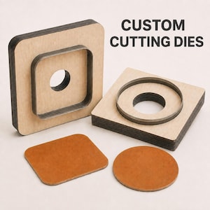 Peut inclure: Deux matrices de découpe personnalisées avec des bases en bois et des lames en métal, l'une carrée et l'autre circulaire, accompagnées d'une pièce de cuir beige carrée et d'une circulaire. Le texte CUSTOM CUTTING DIES est imprimé en noir.