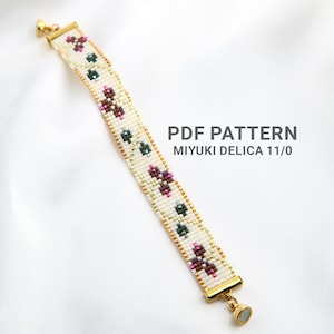 May include: A beaded bracelet with a cream background, featuring a floral pattern in pink, green, and gold. The bracelet has gold-colored clasps and the text "PDF PATTERN MIYUKI DELICA 11/0".