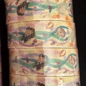 May include: A stack of decorative washi tape rolls. The tape features a repeating pattern of cartoon figures, flowers, and abstract shapes in pastel colors. The rolls are wrapped in clear plastic.