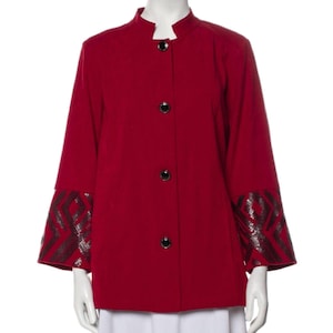 May include: A red jacket with a mandarin collar and three black buttons. The sleeves have a flared design with a geometric pattern in black and silver. The jacket is displayed on a mannequin.