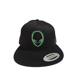 Può includere: Cappellino snapback nero con un design a testa di alieno verde. La testa dell'alieno è ricamata in verde brillante. Il cappellino ha una visiera piatta e una chiusura a scatto sul retro. Marchio Yupoong.