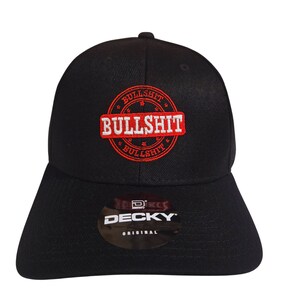 May include: Black baseball cap with a red and white embroidered logo that says "BULLSHIT" in a circle. The logo has a star on each side. The cap has a black label on the back that says "DECKY ORIGINAL".