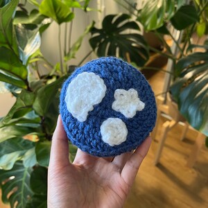 Puede incluir: Una bola de crochet azul con estrellas y nubes de crochet blanco.