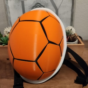 May include: Orange and black soccer ball shaped backpack with adjustable straps.
