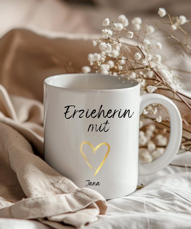 May include: White ceramic mug with black text that reads "Erzieherin mit" and a gold heart. The name "Jana" is written below the heart.