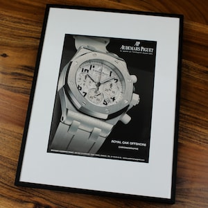 May include: A black and white advertisement for an Audemars Piguet Royal Oak Offshore Chronograph watch. The watch has a silver face with black hands and a black leather band. The text on the advertisement reads "AP Audemars Piguet Le maître de l'horlogerie depuis 1875" and "Royal Oak Offshore Chronographe".