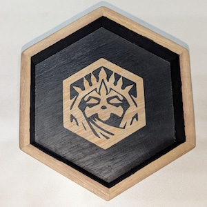 May include: A hexagonal wooden tray with a black stained interior and a natural wood rim. The tray features a carved design of a creature's face with a crown.