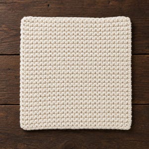 May include: A square, off-white woven cotton trivet with a textured surface. The trivet is made of tightly woven loops, creating a thick, heat-resistant pad. The trivet is approximately 10 inches square.