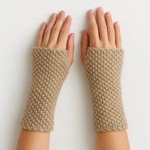May include: A pair of beige knitted fingerless gloves. The gloves are made of a thick, textured yarn and have a ribbed cuff. The gloves are designed to keep the hands warm while leaving the fingers free.