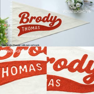 May include: A triangular off-white felt pennant featuring the name Brody in large, textured, rusty red script lettering. Below the name, the word THOMAS is displayed in white capital letters on a rusty red, banner-shaped background.