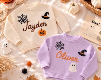 May include: A cream-colored knit sweater with a black spiderweb, a black witch hat, an orange pumpkin, and the name Jayden in brown, alongside a lavender knit sweater with a black spiderweb, a black witch hat, a white ghost, and the name Oliver in orange.
