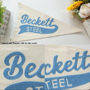 May include: A triangular off-white canvas pennant featuring the embroidered text Beckett STEEL in sky blue. The pennant includes two metal grommets along the left vertical edge for hanging. The design is shown in full and in close-up detail.