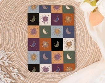 May include: A square decorative item with a celestial patchwork design. Each square features a sun or crescent moon in various colours, including purple, orange, and blue. The item is set on a woven, beige surface.