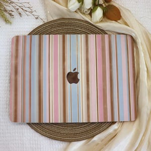May include: A laptop case with a vertical striped pattern in shades of pink, blue, and brown. The Apple logo is visible in the center. The case is on a round, woven placemat.