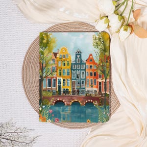 Peut inclure: Une impression d'art colorée représentant une scène de canal avec des bâtiments aux couleurs vives, jaunes, bleus, oranges et verts. L'œuvre présente un pont avec des vélos et des arbres, sur fond de ciel et d'eau bleu clair.