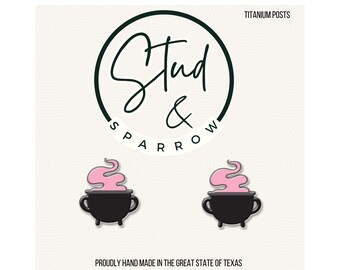 May include: A pair of black cauldron earrings with pink smoke detail. The earrings are set against a white background with the text "Stud & Sparrow" in a circular design. The text "Titanium Posts" is also visible.