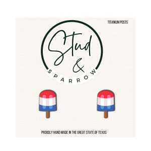 May include: A pair of popsicle-shaped stud earrings with red, white, and blue stripes, and a brown stick. The earrings are displayed on a white background with the text "Stud & Sparrow" and "Proudly hand made in the great state of Texas."