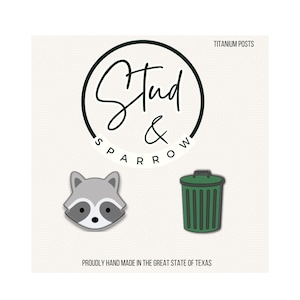 May include: Stud & Sparrow logo with two stud earrings: a raccoon face and a green trash can. The text "Titanium Posts" is above the logo, and "Proudly Hand Made in the Great State of Texas" is below.