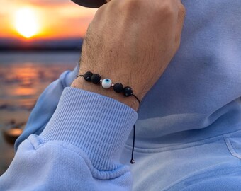 May include: A black string bracelet with black lava rock beads and a white evil eye charm.