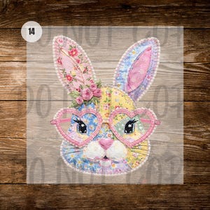 Puede incluir: Una colorida cara de conejo de retazos con gafas en forma de corazón. Las orejas y la cara del conejo están hechas de tela estampada floral en rosa, amarillo y azul. Un pequeño grupo de rosas rosas adorna la parte superior de la cabeza. El número 14 está en un círculo blanco.