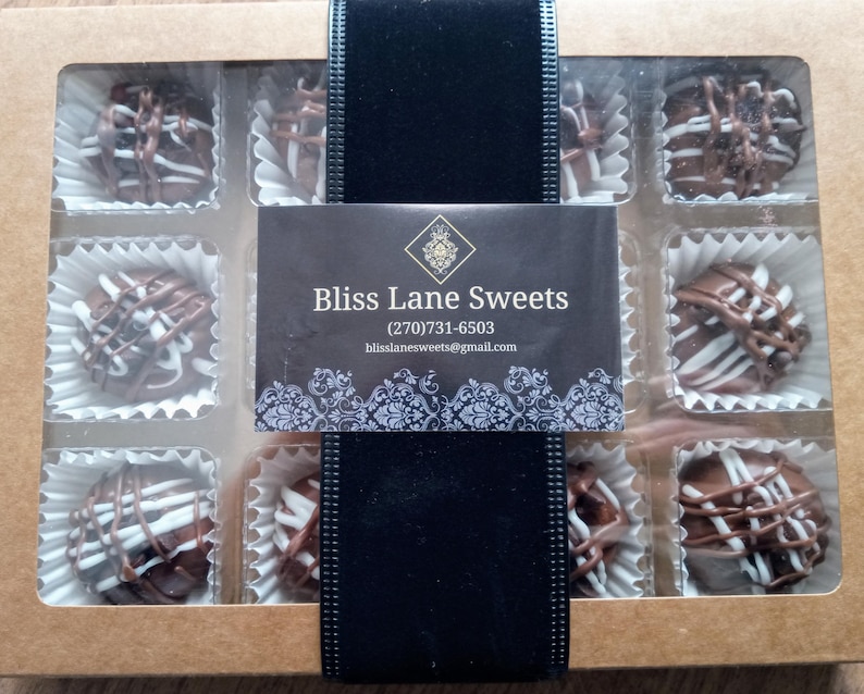 Pu&ograve; includere: Una scatola di nove tartufi al cioccolato con vortici bianchi e marroni. La scatola &egrave; etichettata "Bliss Lane Sweets" con un numero di telefono e un indirizzo email.