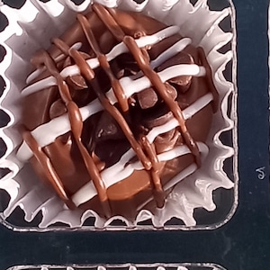 Pu&ograve; includere: Un singolo tartufo al cioccolato con cioccolato bianco e marrone glassato sopra, seduto in un pirottino di carta bianco.