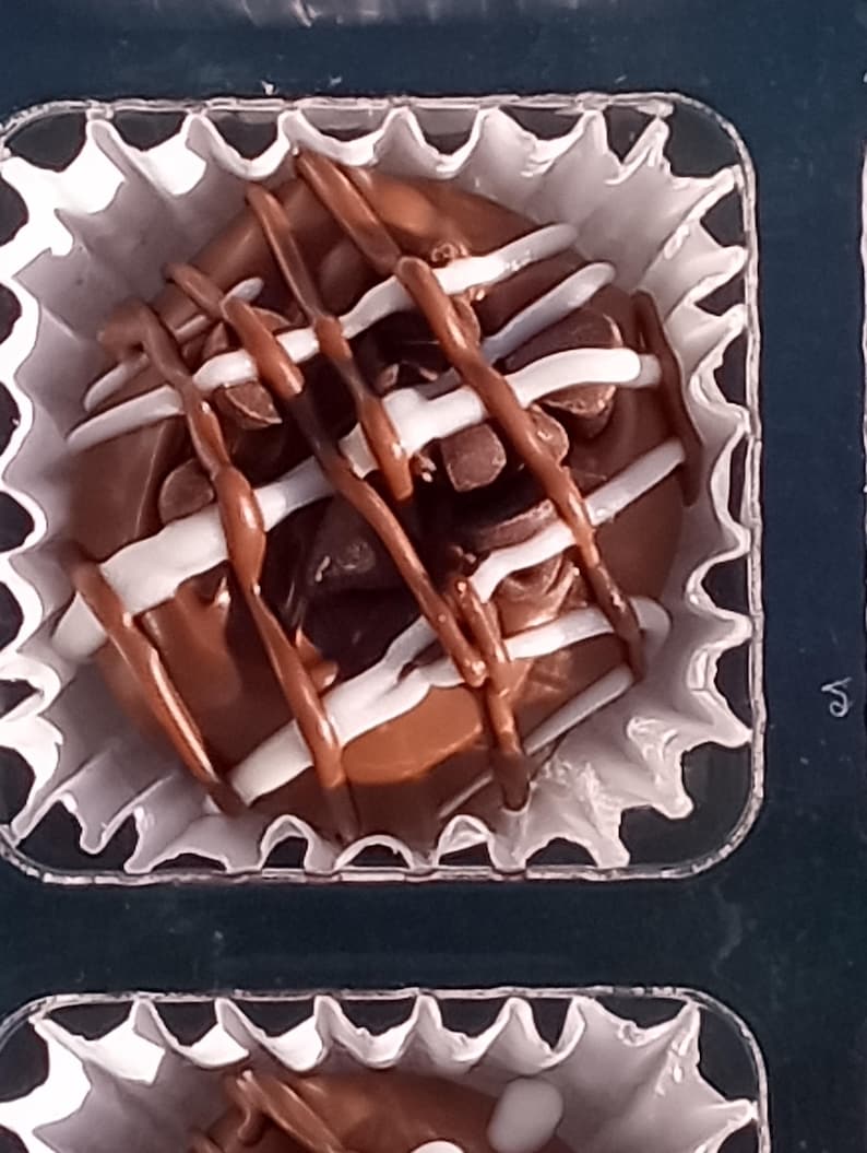 Pu&ograve; includere: Un singolo tartufo al cioccolato con cioccolato bianco e marrone glassato sopra, seduto in un pirottino di carta bianco.