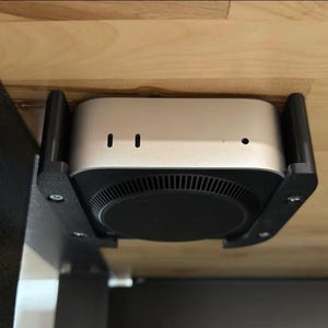 May include: An Apple TV device in silver, mounted to the underside of a wooden table using a black bracket.