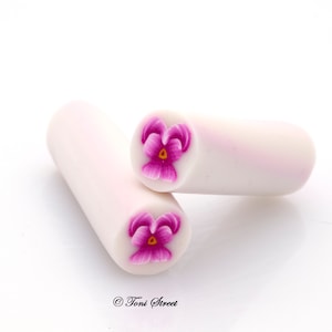 May include: Two white polymer clay cylinders with a pink flower design on each end. The flowers have a yellow center and pink petals.
