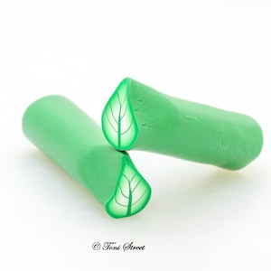 Puede incluir: Dos canes de arcilla polimérica verde con un diseño de hoja cortado en ellas. Las canes están dispuestas de modo que los diseños de hojas se enfrentan.