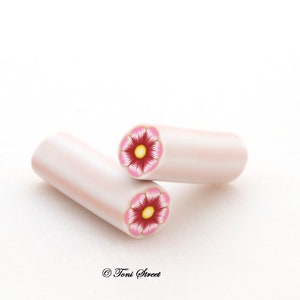 Könnte beinhalten: Zwei weiße Polymer Clay Perlen mit rosa und gelben Blumendesigns. Die Perlen sind etwa 2,5 cm lang.
