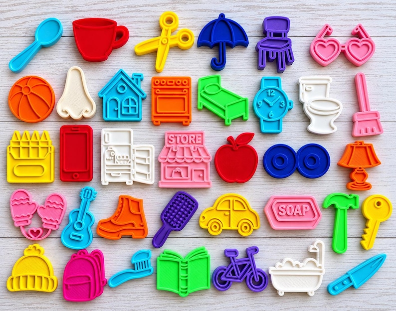 May include: A collection of colorful plastic cookie cutters in various shapes including a spoon, cup, scissors, umbrella, chair, heart glasses, ball, nose, house, oven, bed, watch, toilet, broom, crayons, phone, fridge, store, apple, lamp, mittens, guitar, boot, brush, car, soap, hammer, key, hat, backpack, toothbrush, book, bicycle, bathtub, and knife.