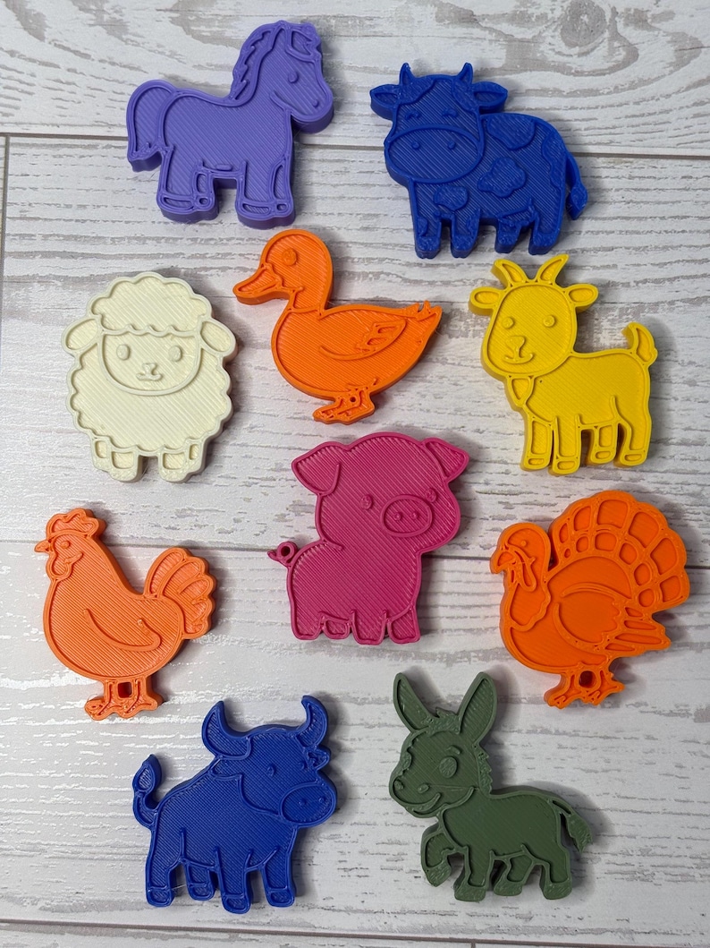 May include: A collection of ten plastic animal-shaped cookie cutters in various colors including purple, blue, white, orange, yellow, pink, and green. The set features a horse, cow, sheep, duck, goat, chicken, pig, turkey, bull, and donkey.