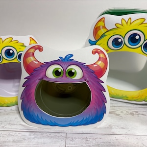 May include: Three colorful monster-shaped containers. The containers have large eyes, horns, and open mouths. The monsters are yellow, purple, and blue with rainbow accents. The containers are likely for storage or decoration.