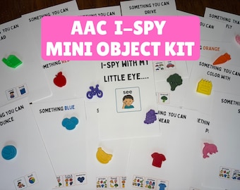 May include: An AAC I-Spy mini object kit featuring multiple white cards with printed text prompts and small colorful plastic figures. The cards include phrases like Something You Can Read, Something Blue, and I-Spy With My Little Eye, paired with miniature items such as a red apple, blue bicycle, yellow banana, green broccoli, and purple grapes.