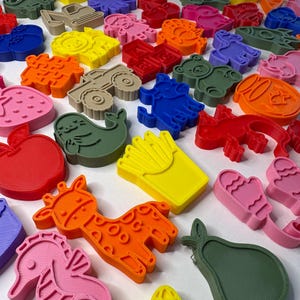 May include: A collection of colorful plastic cookie cutters in various shapes including animals, food items, vehicles, and letters. The assortment features vibrant shades of red, orange, yellow, green, blue, and pink, all arranged together.